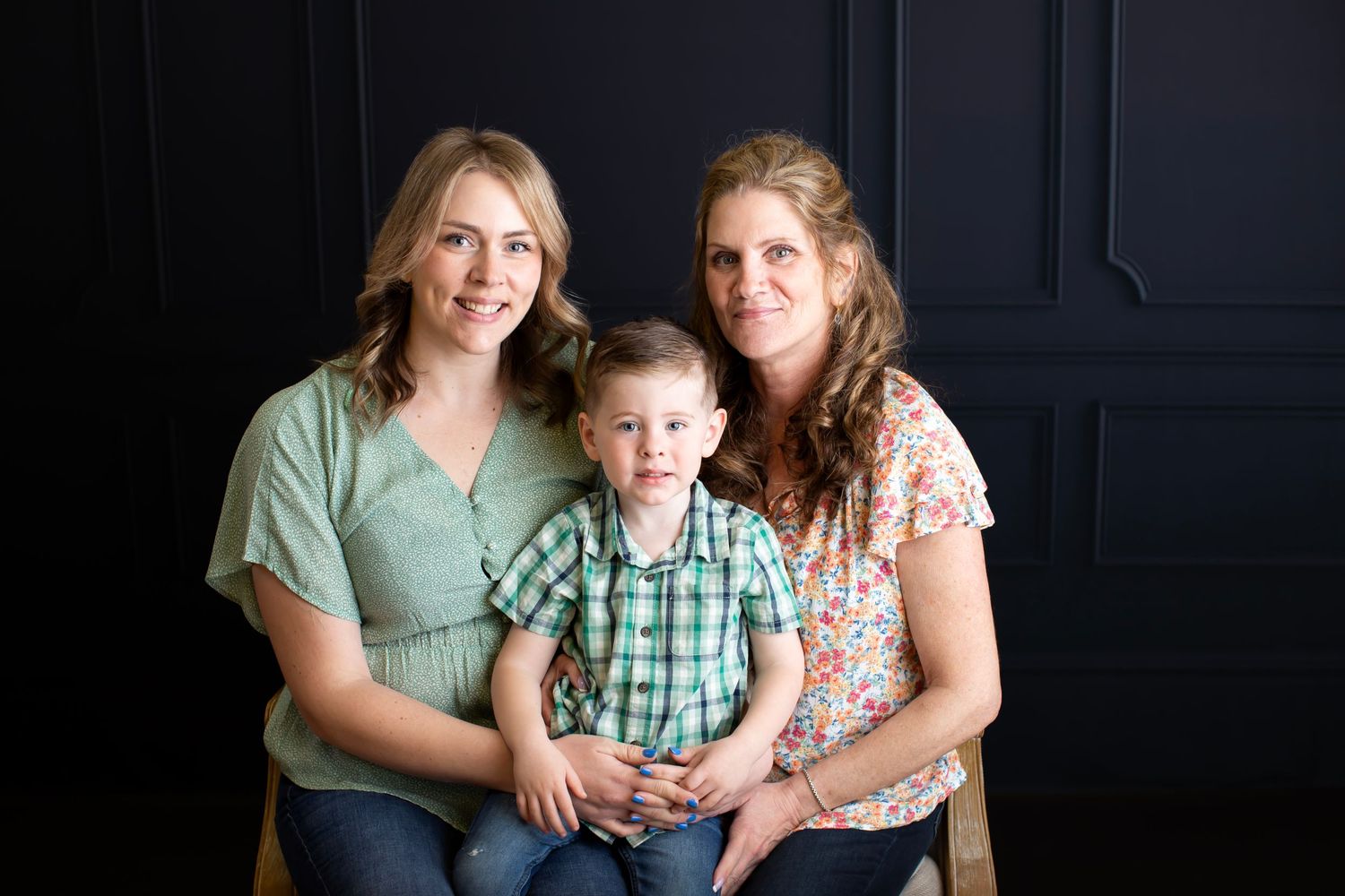 Studio portrait against dark wall featuring casual family grouping in coordinated outfits.