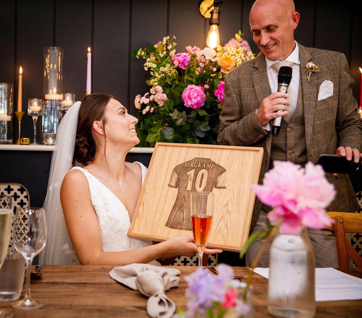 Wedding reception table settings with wooden decor and pink floral arrangements.