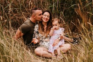 A happy family shares intimate moments while sitting in tall grass outdoors.