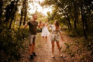Three people jumping with joy on a forest trail during sunset.