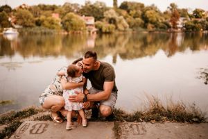 Family sharing a tender moment by a serene lake with houses visible on the opposite shore.