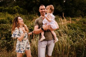 Family outdoor portrait in matching floral outfits among tall summer grasses.