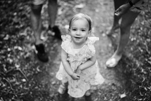 Black and white photo of toddler in ruffled dress smiling outdoors.