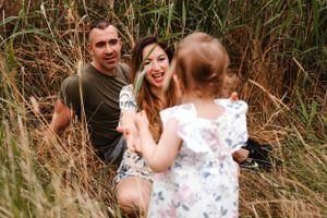 Family enjoying a playful moment together in tall grass during sunset.