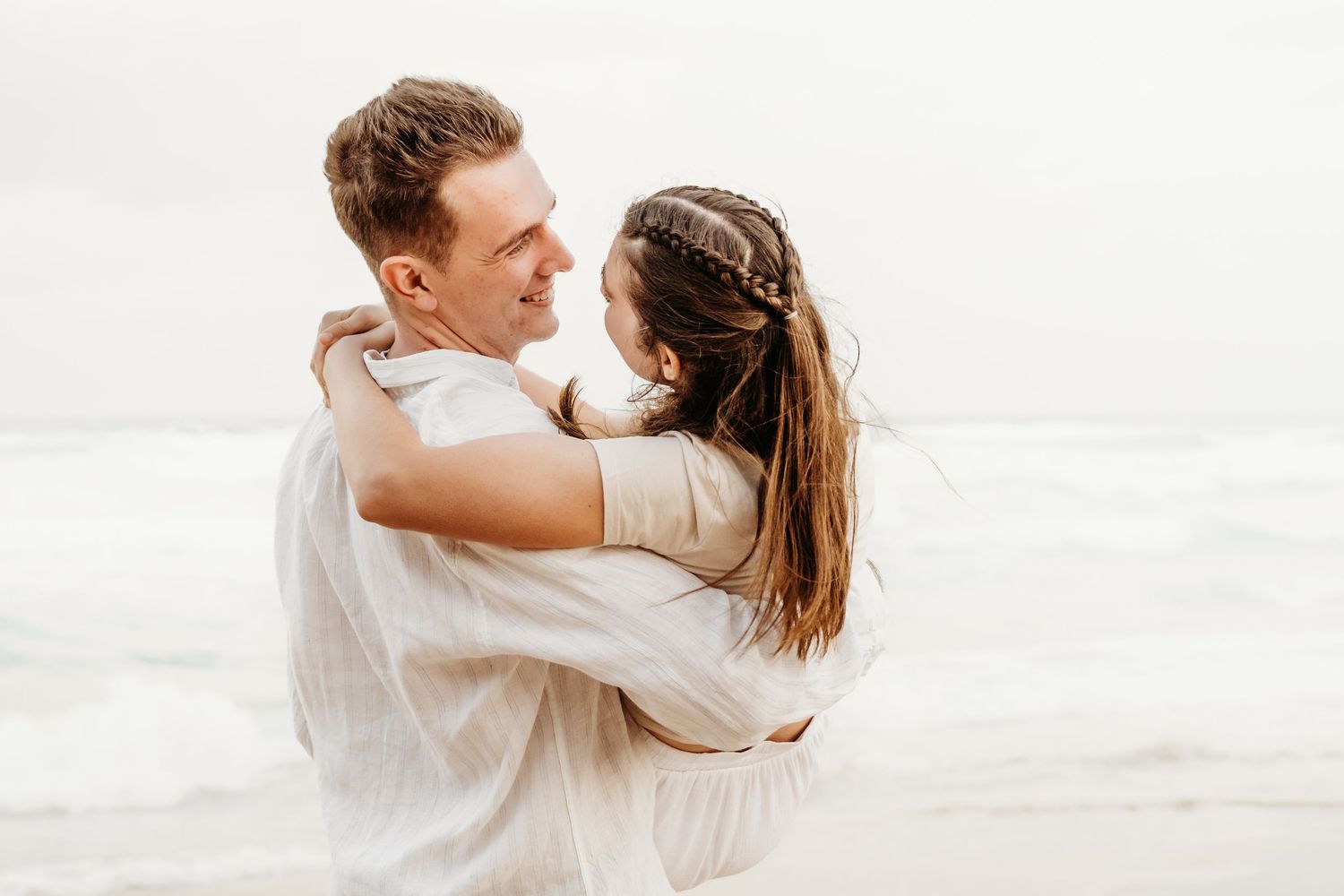 A tender embrace between a couple on a misty beach with waves in the background.