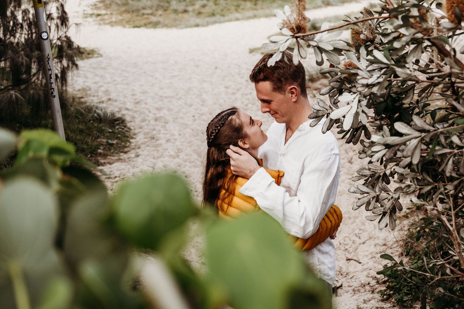 A couple shares an intimate moment along a nature path surrounded by foliage.