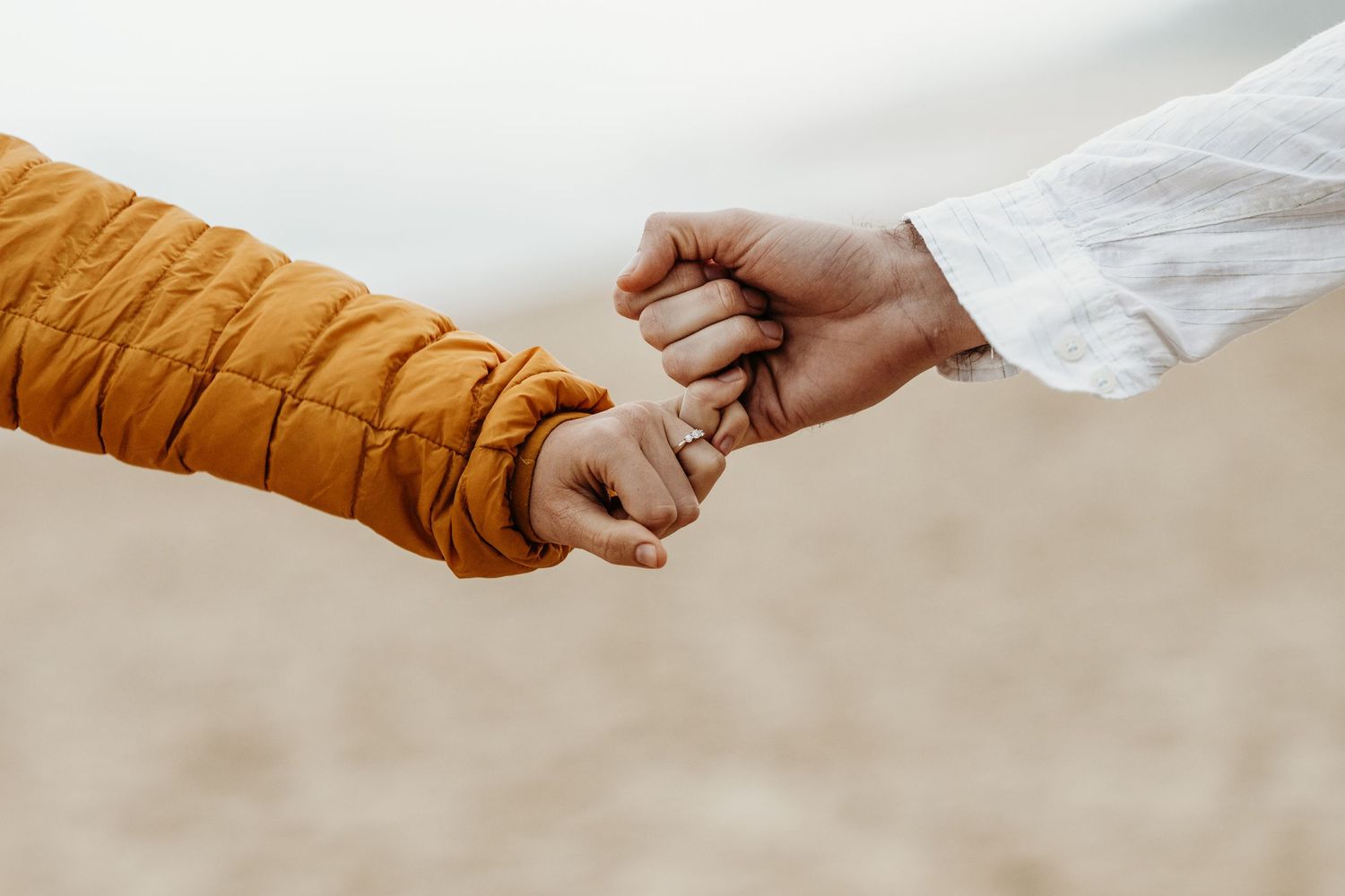 Two hands reaching towards each other, one wearing orange and one wearing white.
