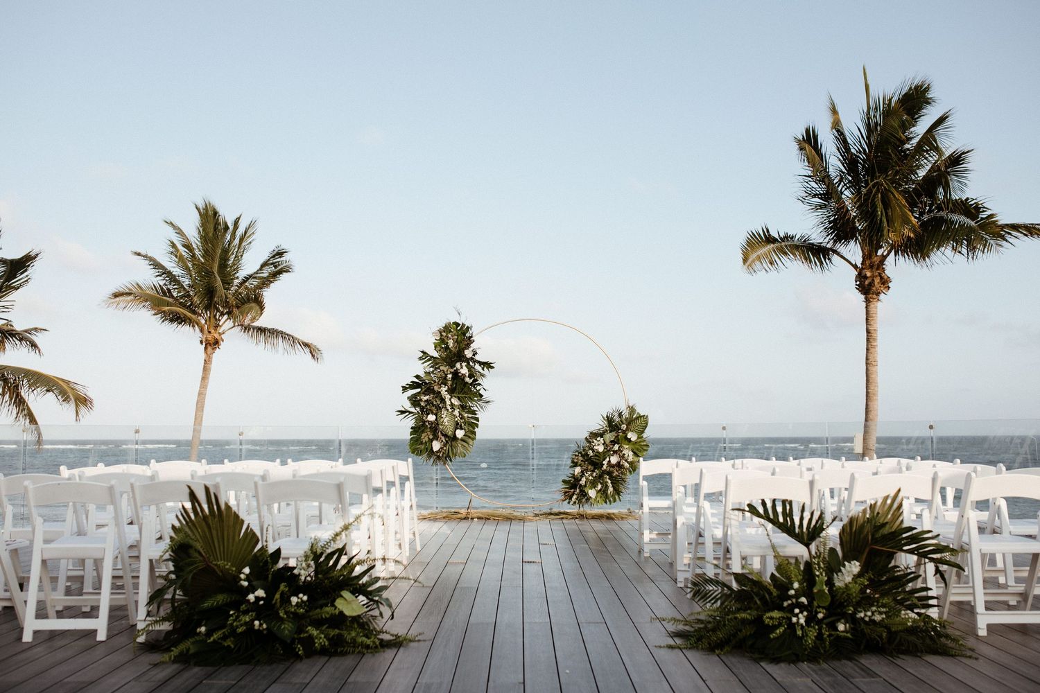 Tropical beach wedding setup with white chairs and palm trees against ocean backdrop. Wedding photographer in Mexico Riviera Maya
