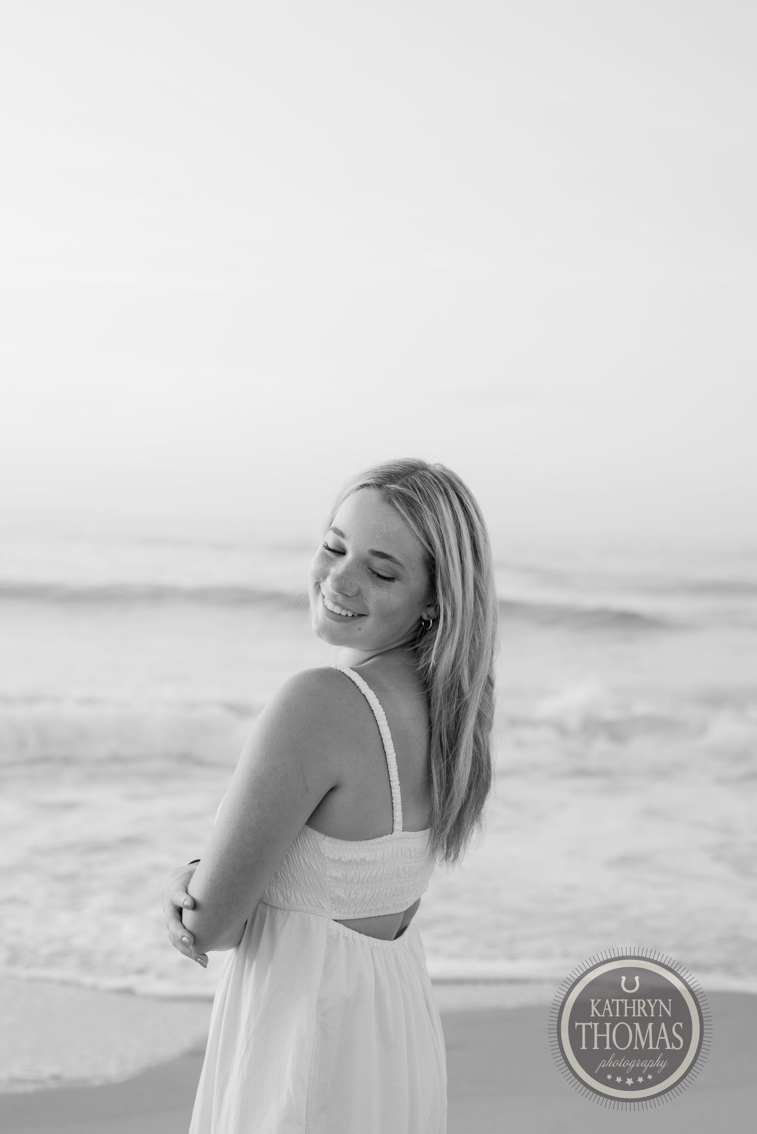 Black and white beach portrait showing a joyful expression and casual pose.