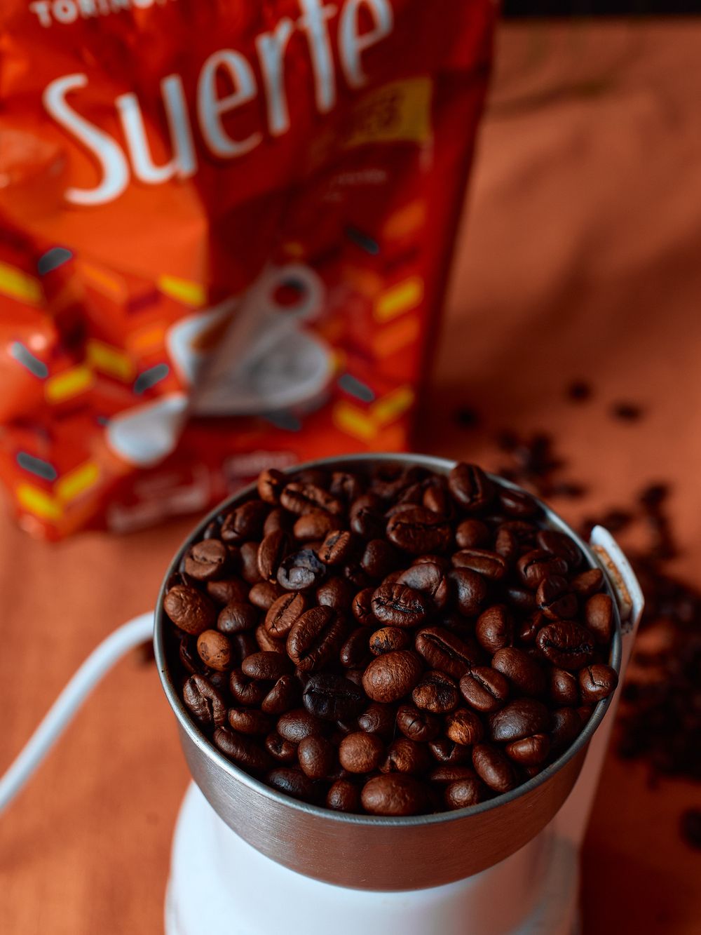 Coffee beans fill a metal grinder container next to a Suerte coffee package.