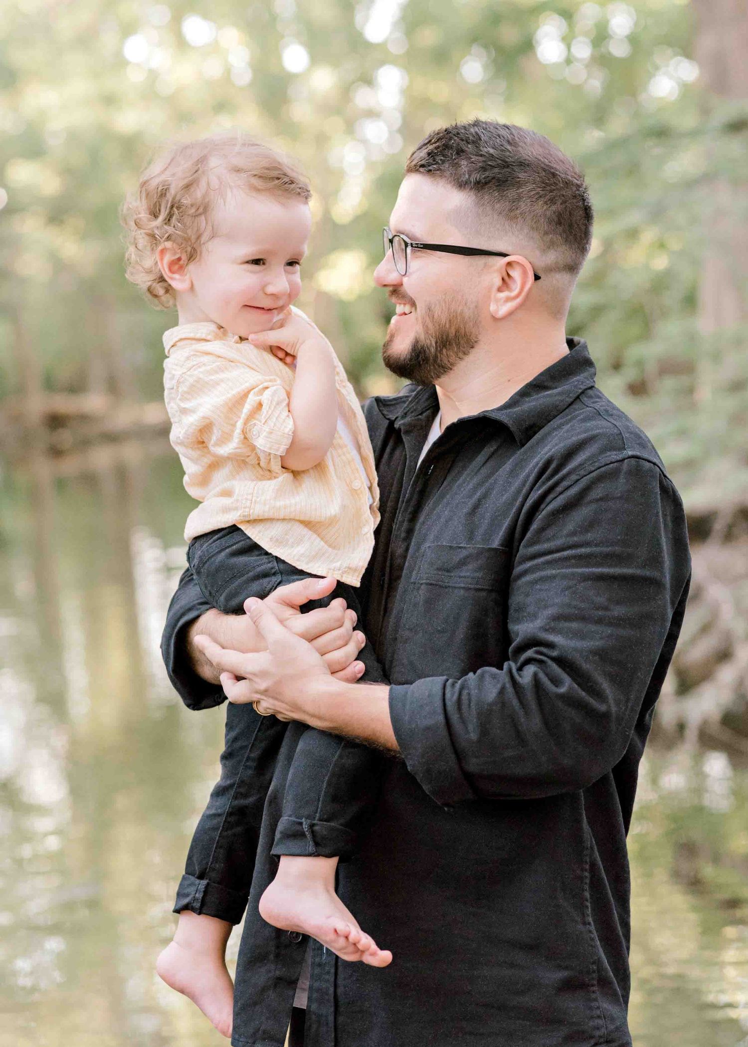Candid father and child moment captured against a serene creek background.