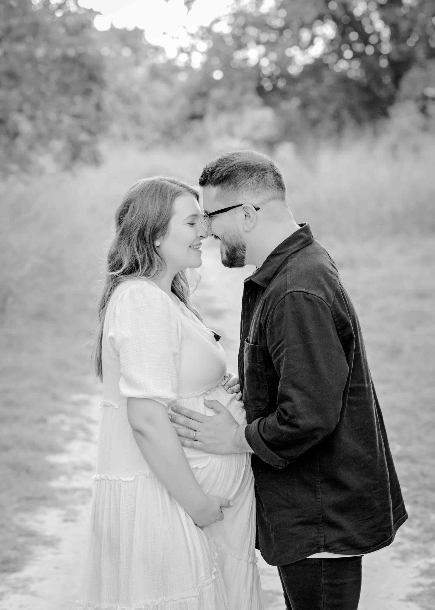 An intimate black and white maternity portrait capturing a tender moment on a nature path.