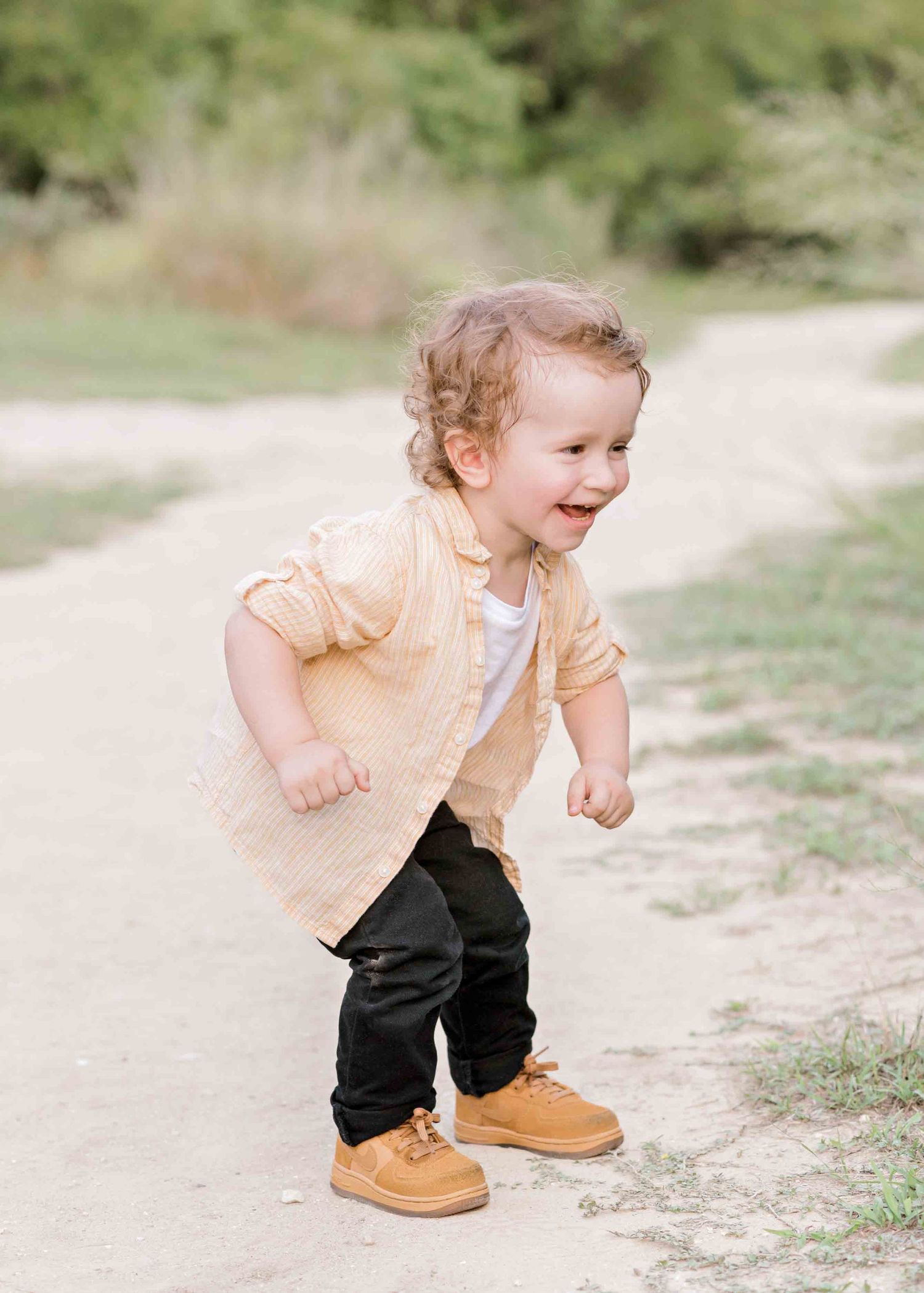 A joyful toddler in a peach jacket and boots runs playfully on a dirt path.