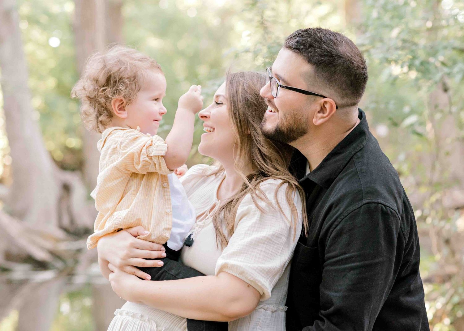 A joyful family moment captured by a creek with tall trees in the background.
