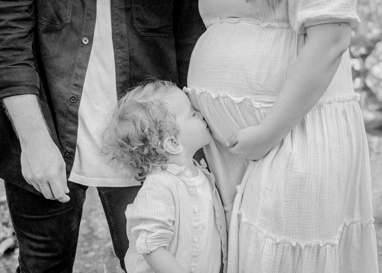 Black and white intimate maternity photo showing a tender family moment by the water.