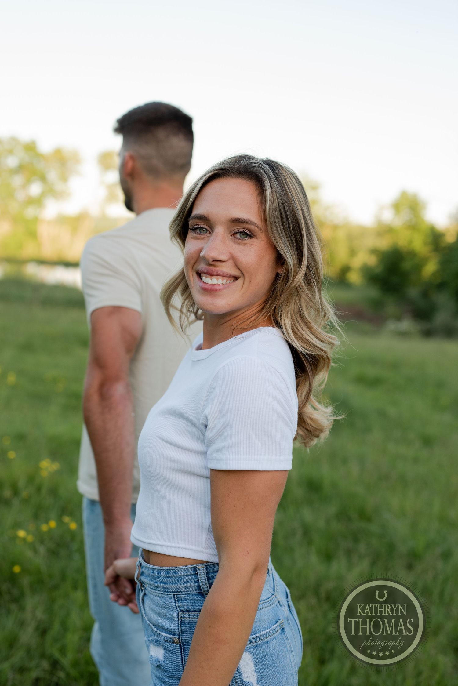 A couple in casual white t-shirts and jeans posing in a sunny meadow with wildflowers.