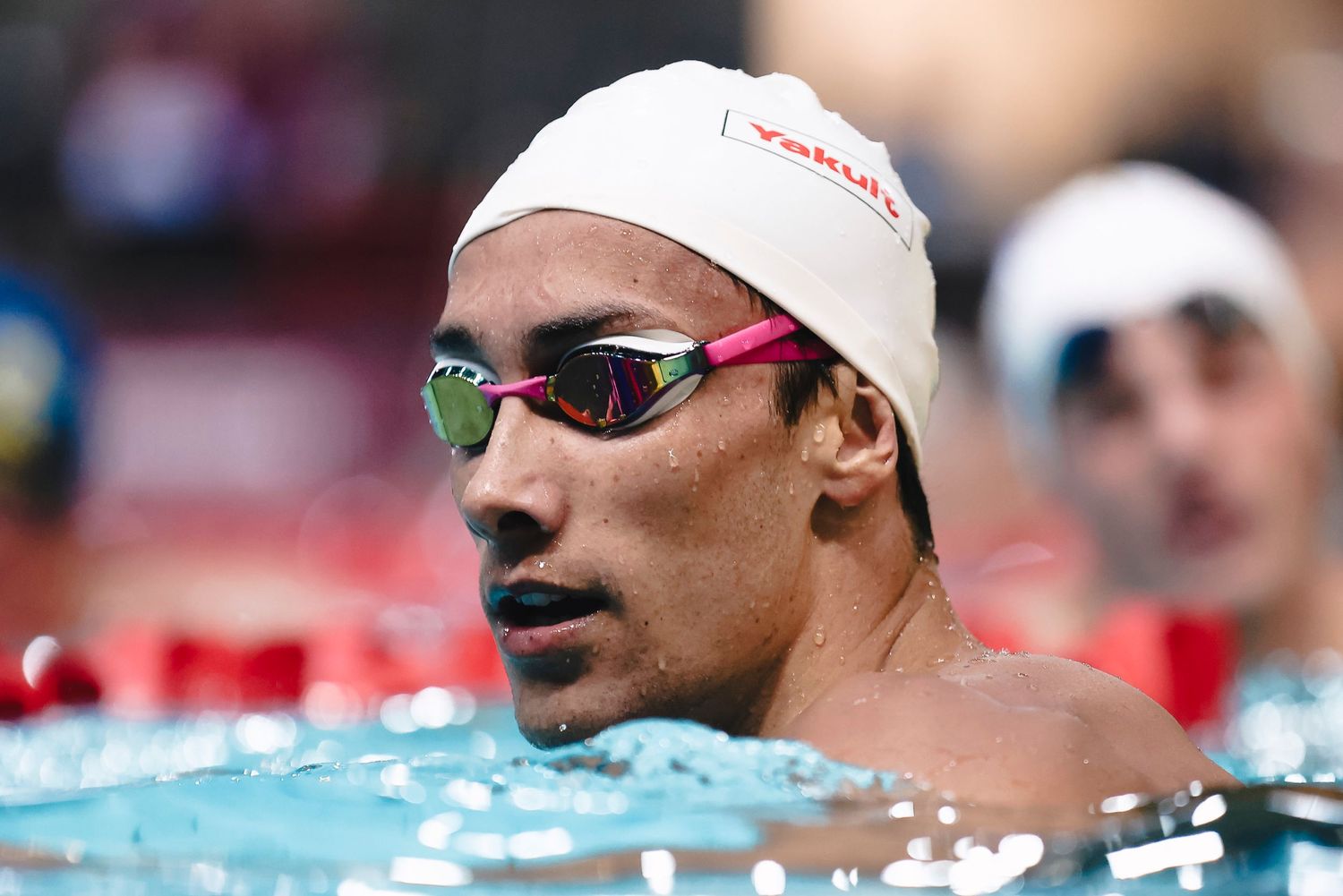 Competitive swimmer wearing cap and goggles at pool during swimming event.