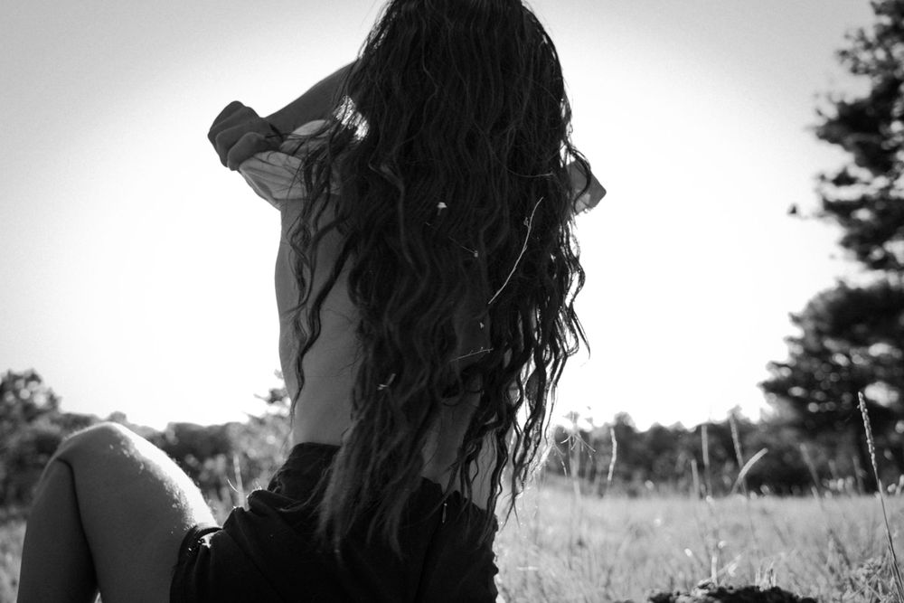 Artistic black and white photo of long dark hair flowing in the wind against nature backdrop.