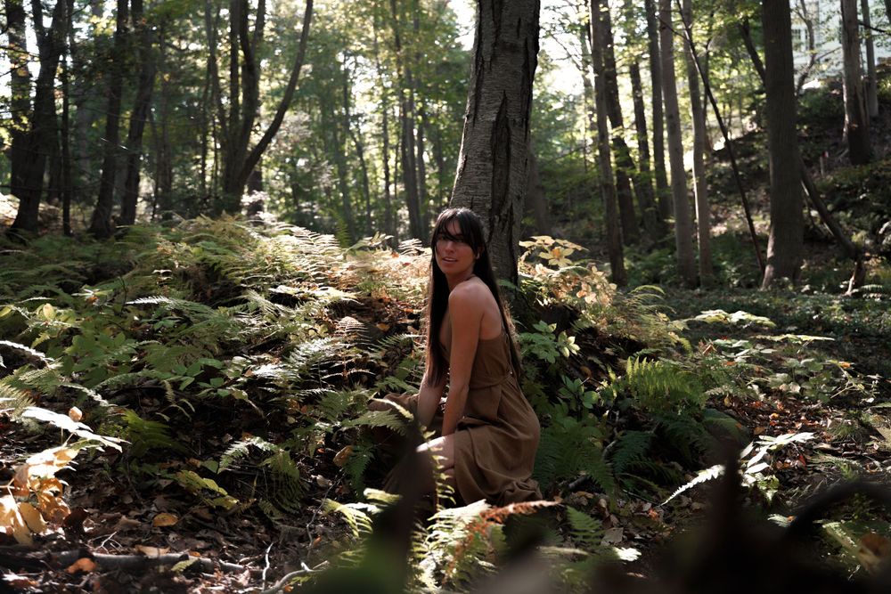 Figure sitting among mossy rocks in sunlit forest setting.