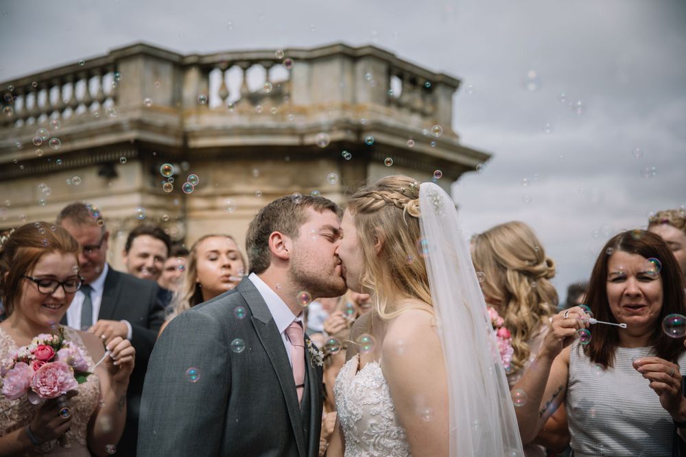 A tender moment between newlyweds surrounded by guests outside a historic building.