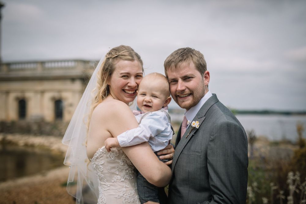 A joyful wedding portrait with a baby against a scenic coastal backdrop.