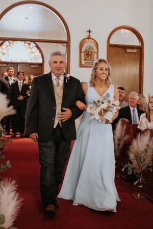 Wedding party members process through church decorated with pampas grass and religious artwork.