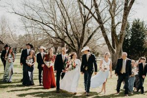 Wedding party poses casually outdoors with mix of formal wear and western style elements.