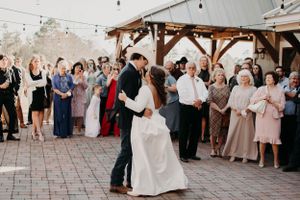 Couple shares a romantic dance moment as wedding guests watch from the sides under string lights.