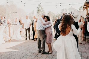 Wedding guests dancing in pairs on outdoor brick patio under string lights and wooden beams.