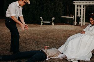 A couple shares a playful moment on a lawn with a white gazebo and benches in the background.