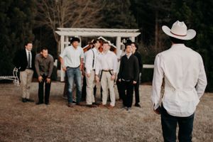 A person in western attire watches a group gathered by a white garden pergola.