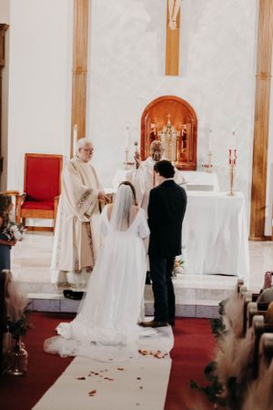 A Catholic wedding ceremony with a priest officiating at an ornate church altar.