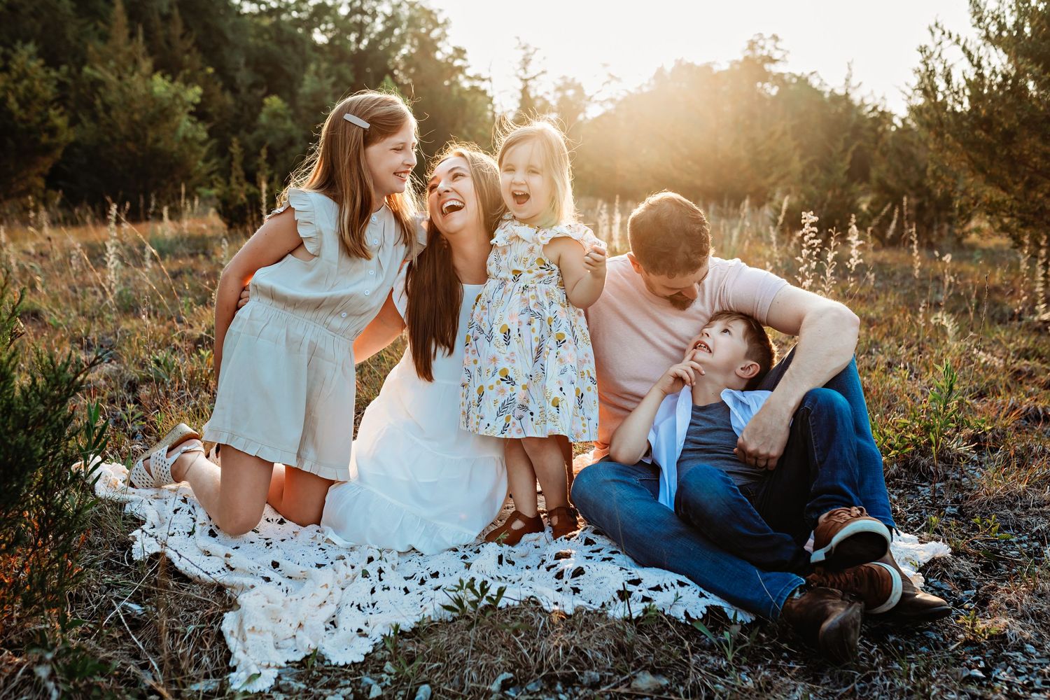 A family photo session outdoors with everyone laughing together on a blanket.