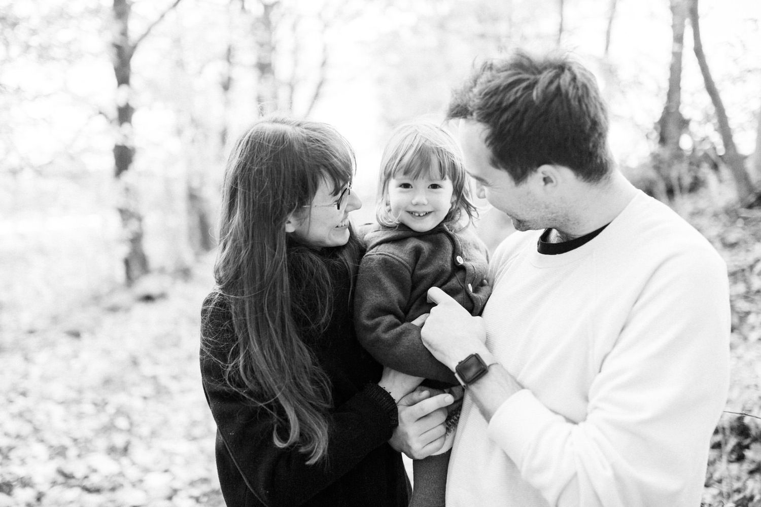 Black and white family portrait showing tender moment outdoors in nature with fallen leaves.