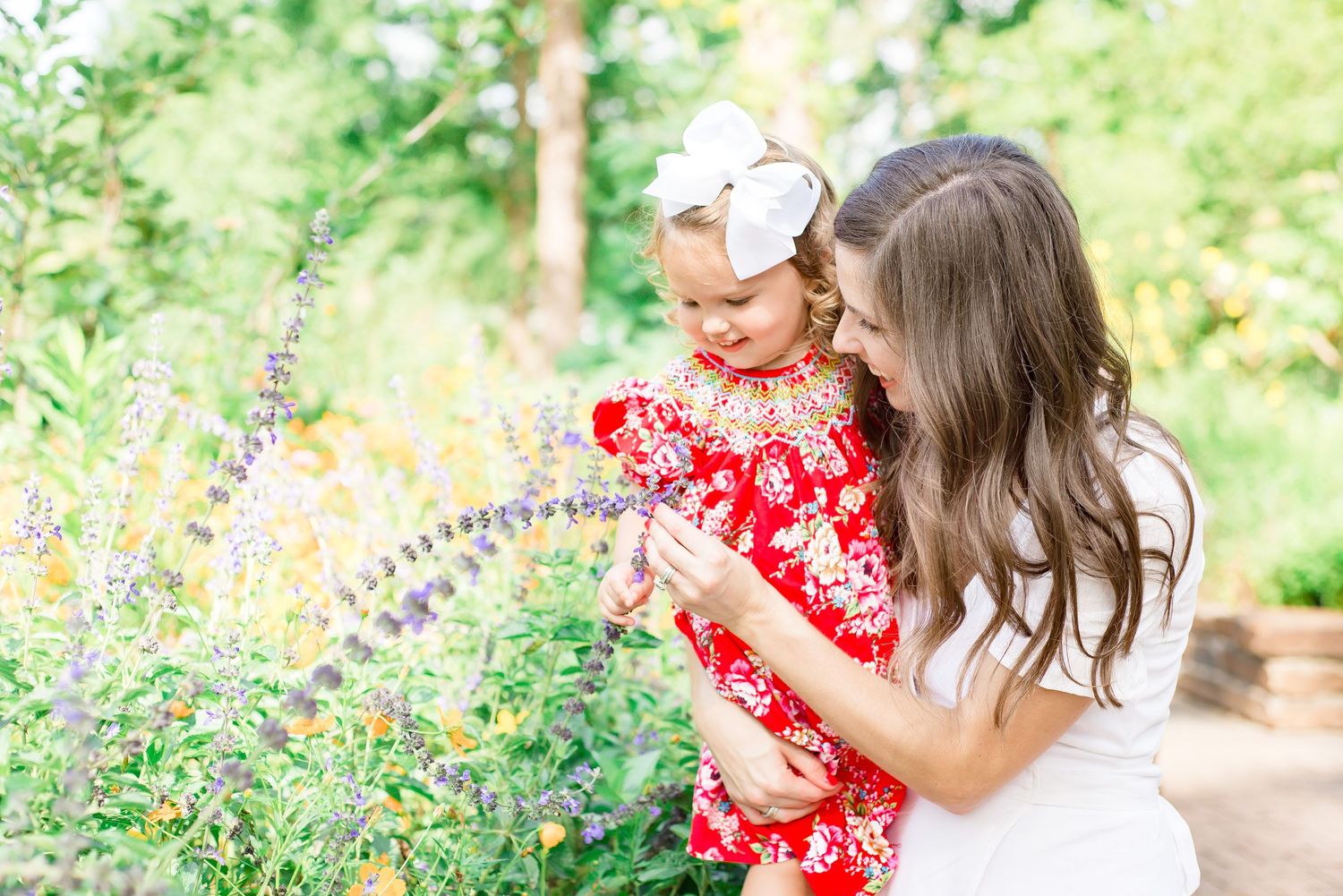 Family wearing white and red outfits poses together in a sunny garden with wildflowers.
