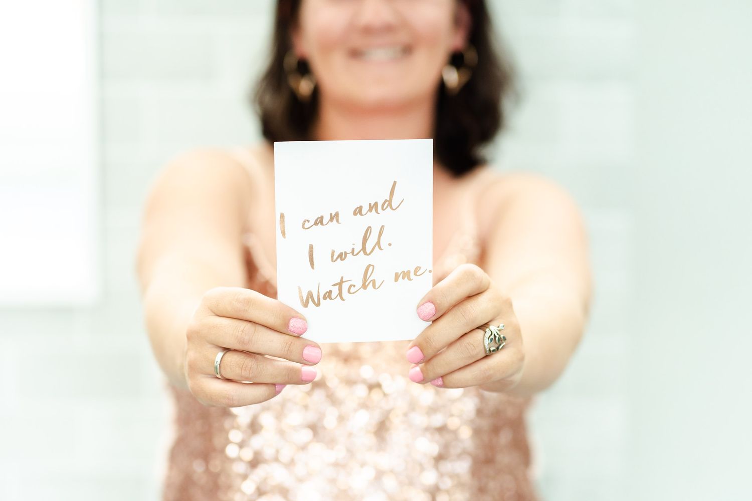 Hands holding motivational card with gold text against white background.