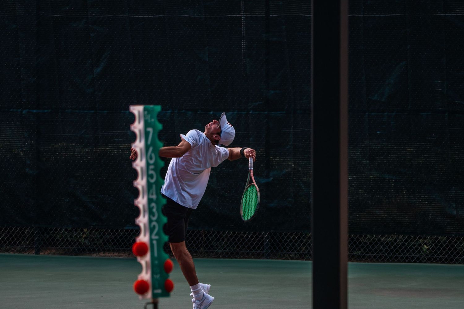 A tennis player serves at night on an illuminated court.