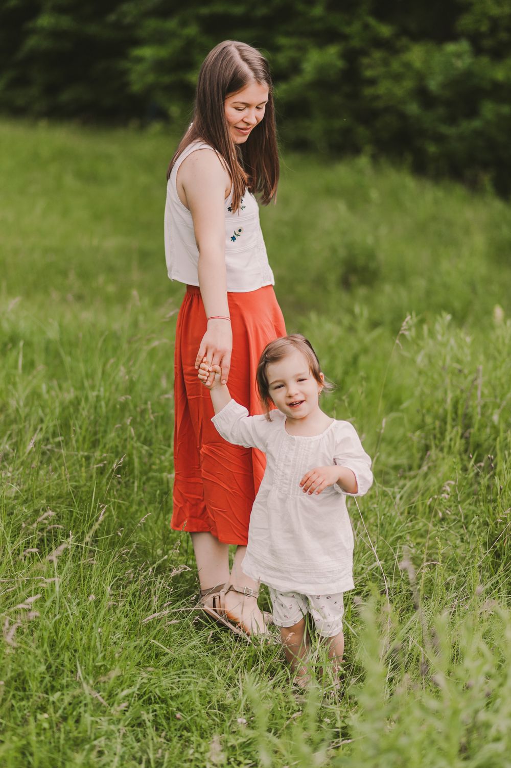 Mother and child walking together through a lush green meadow on a sunny day.