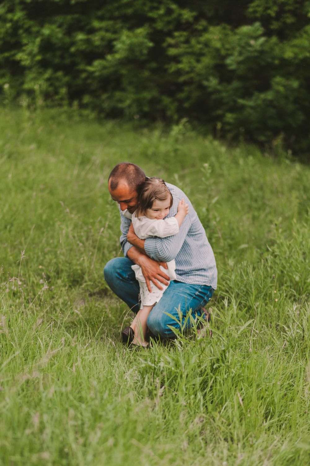 Parent and child sharing a tender moment while sitting in tall grass outdoors.