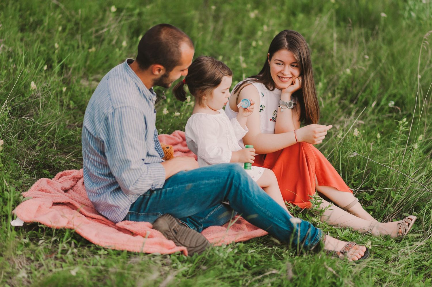 Family enjoying a picnic and playtime on a blanket in a grassy field.