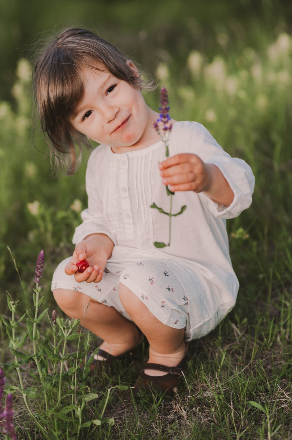 Child exploring nature while crouching near purple flowers in a grassy field.