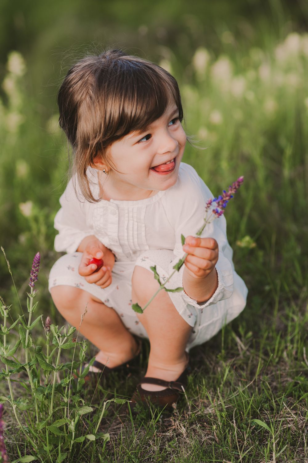 Child examining wildflowers while crouching in a sunlit meadow.