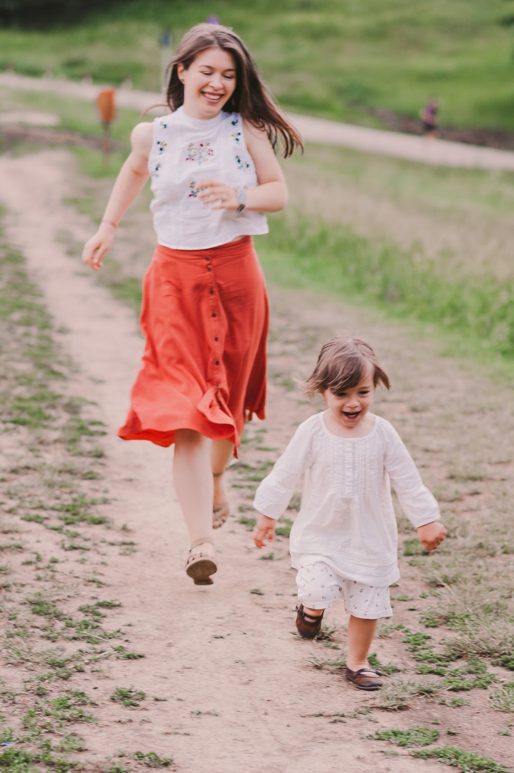 People running and laughing together on a dirt path through green fields.