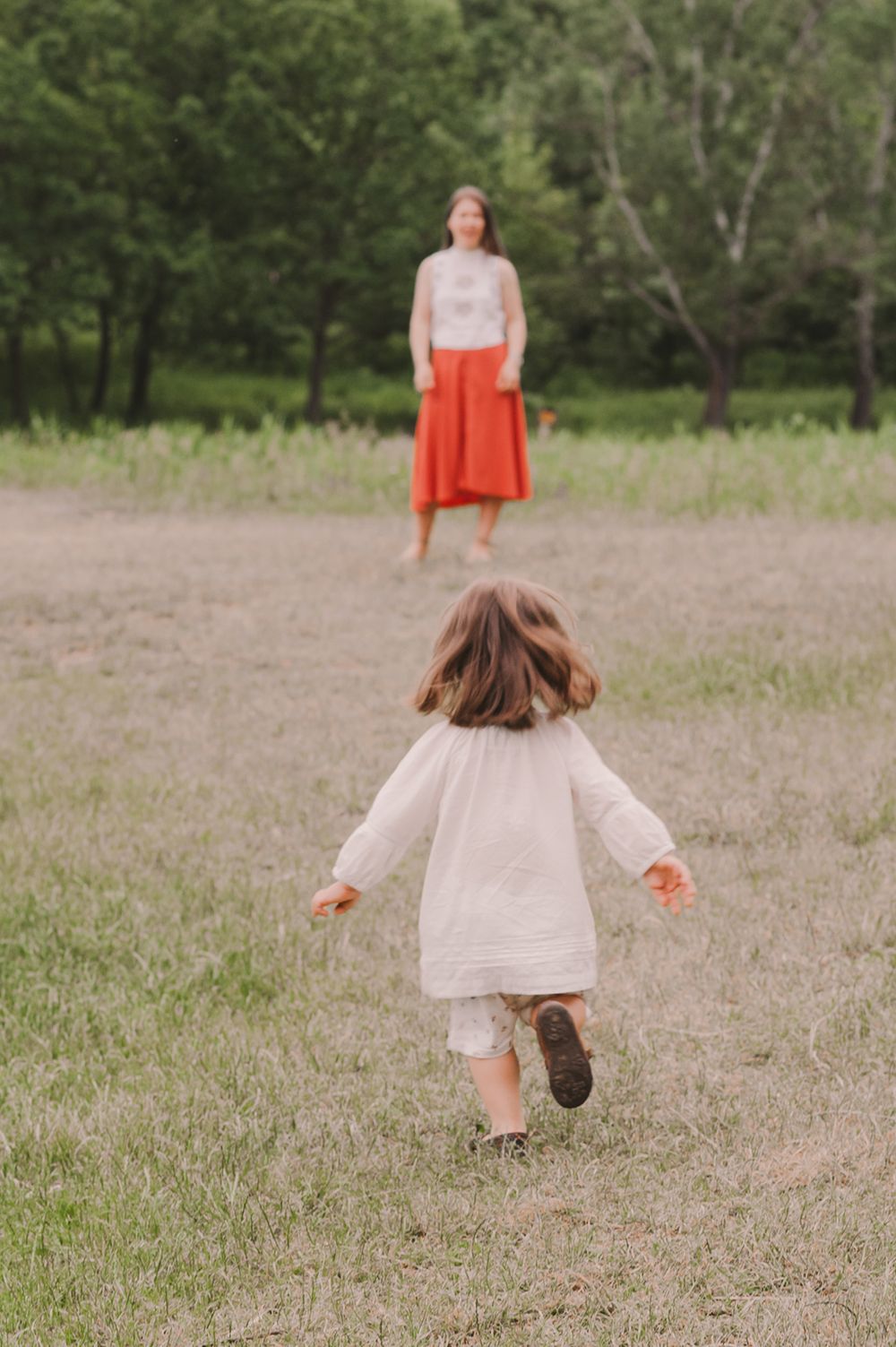 A child in a white dress runs through a grassy field on a sunny day.