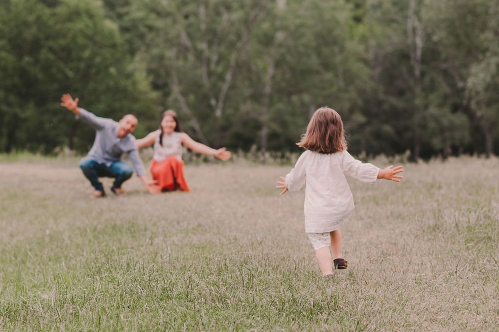 People playing and running together in a grassy field surrounded by trees.