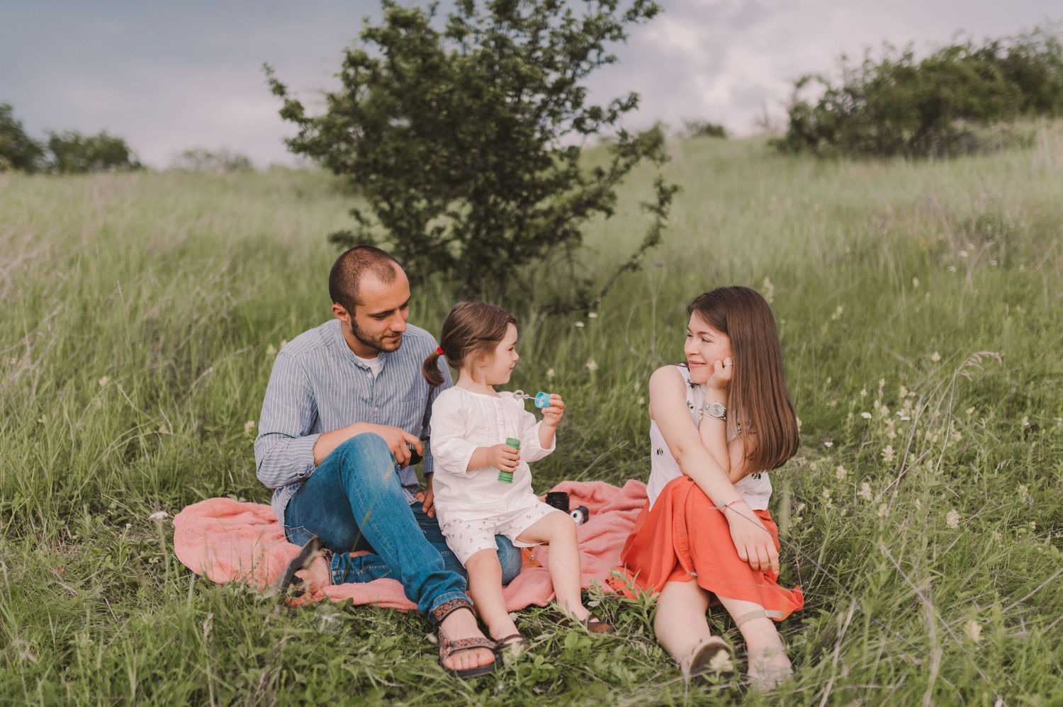 Family members relax together on a grassy hillside during a sunny afternoon.
