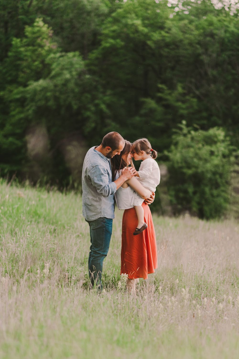 Family sharing intimate moments together in a tall grass field during golden hour.