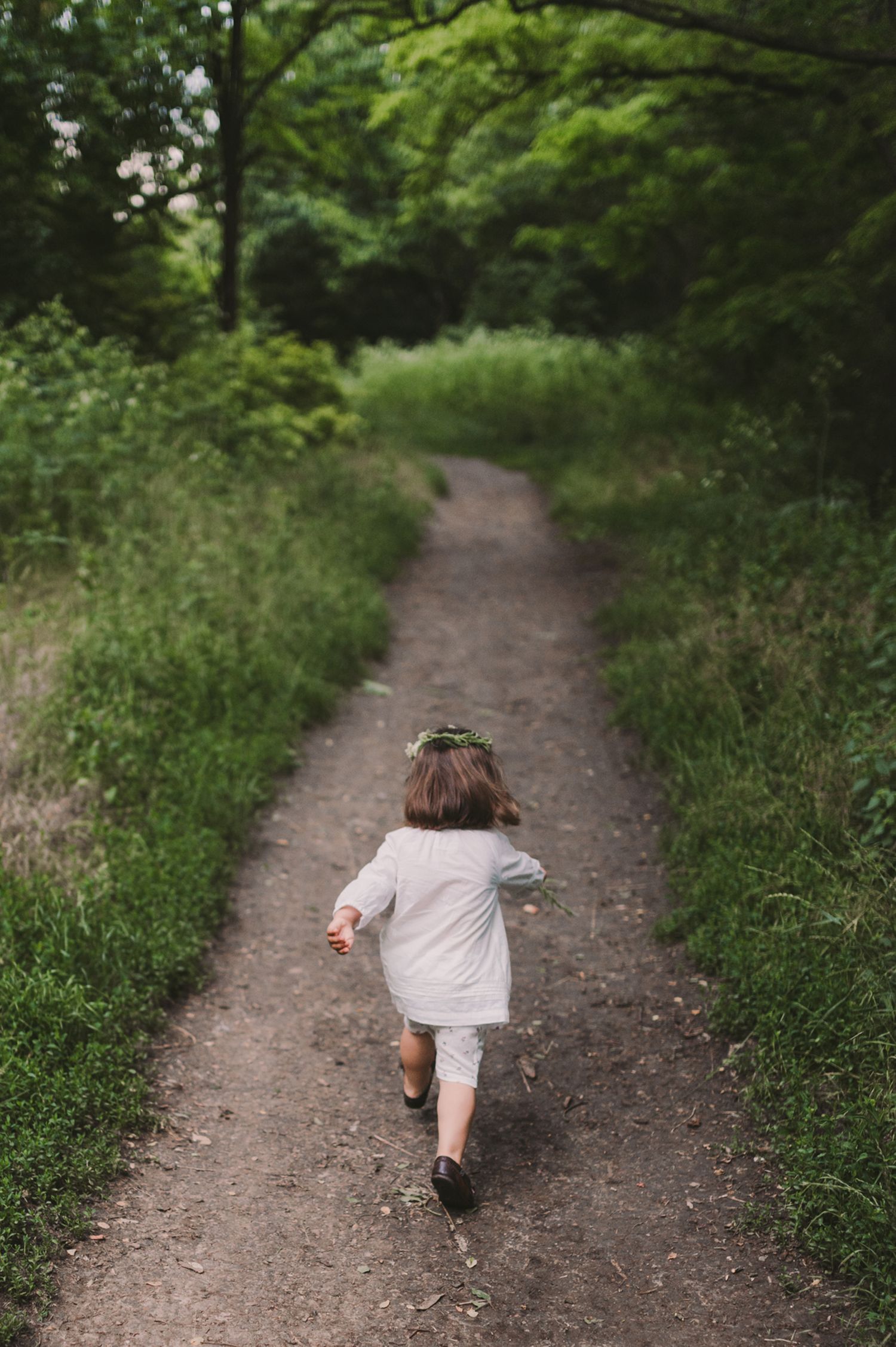Child walking along a tree-lined dirt path on a summer day.