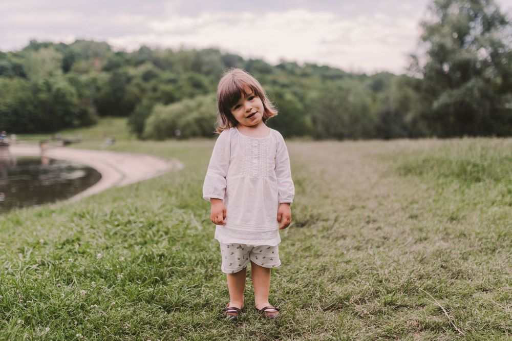Small child standing in a grassy field wearing a light colored dress.