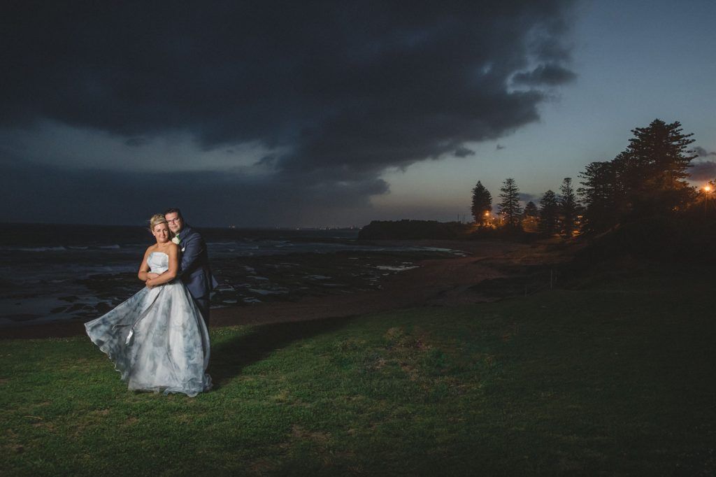Dramatic wedding portraits captured against a moody evening sky near the coastline.